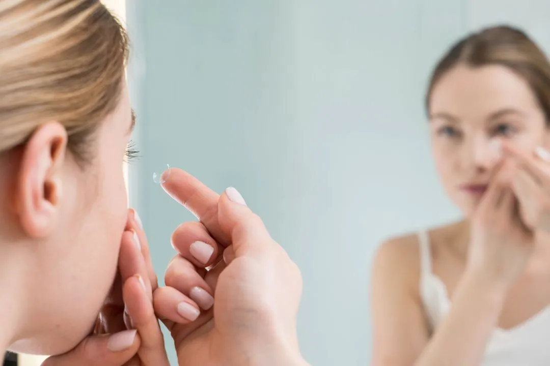 Woman inserting contact lens while looking in mirror