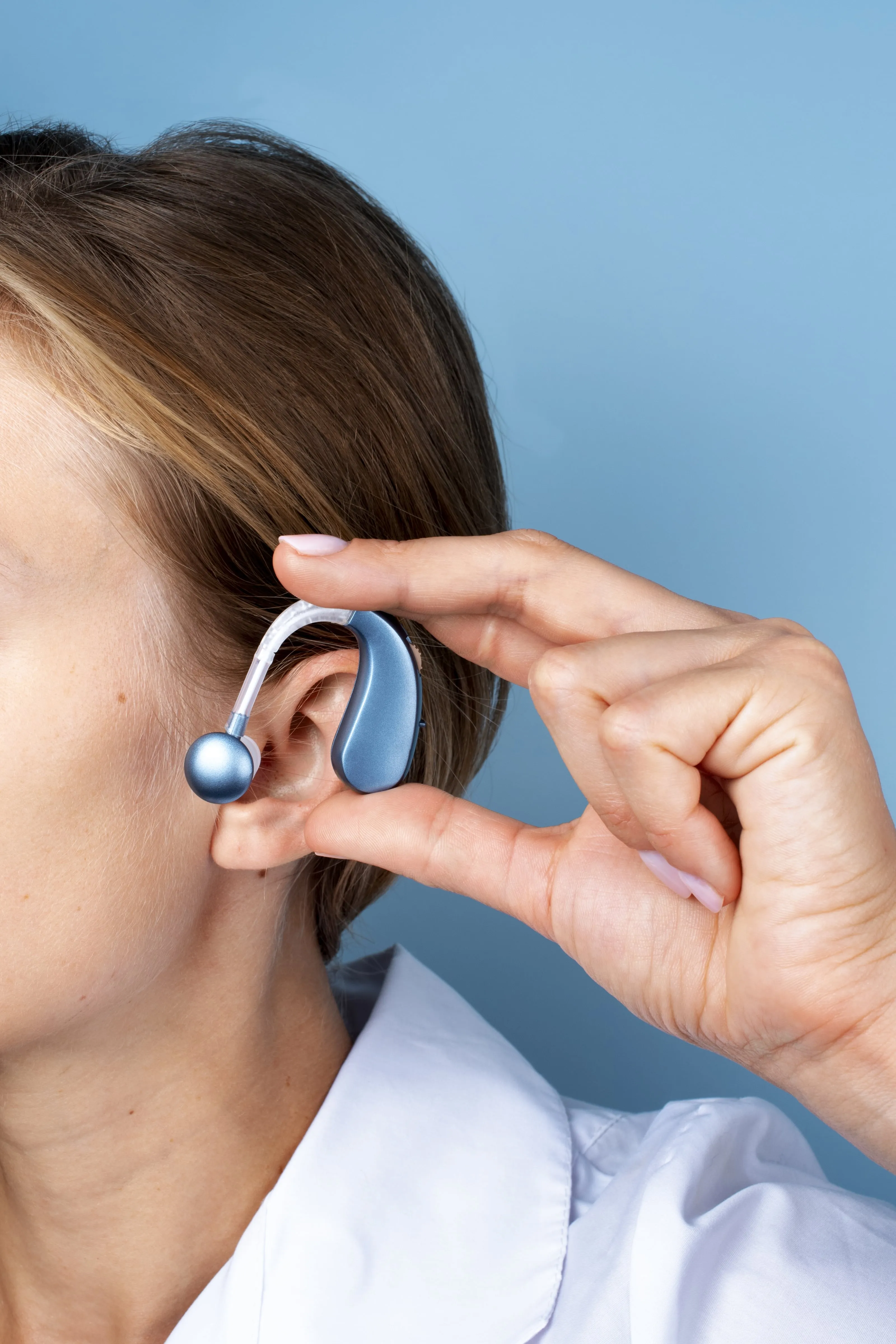 Blue hearing aid being adjusted on person's ear against blue background