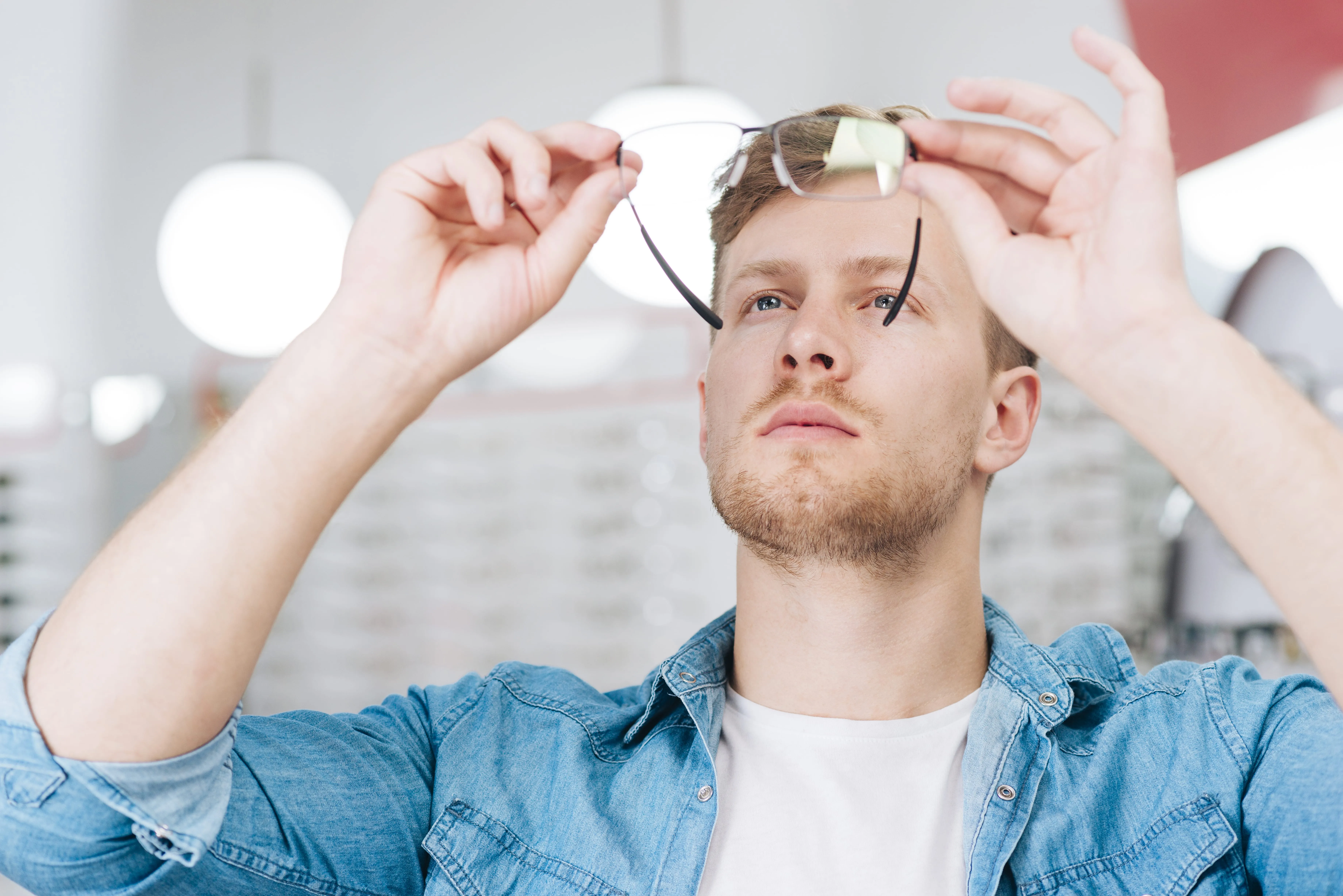 Person in denim shirt adjusting glasses with thoughtful expression