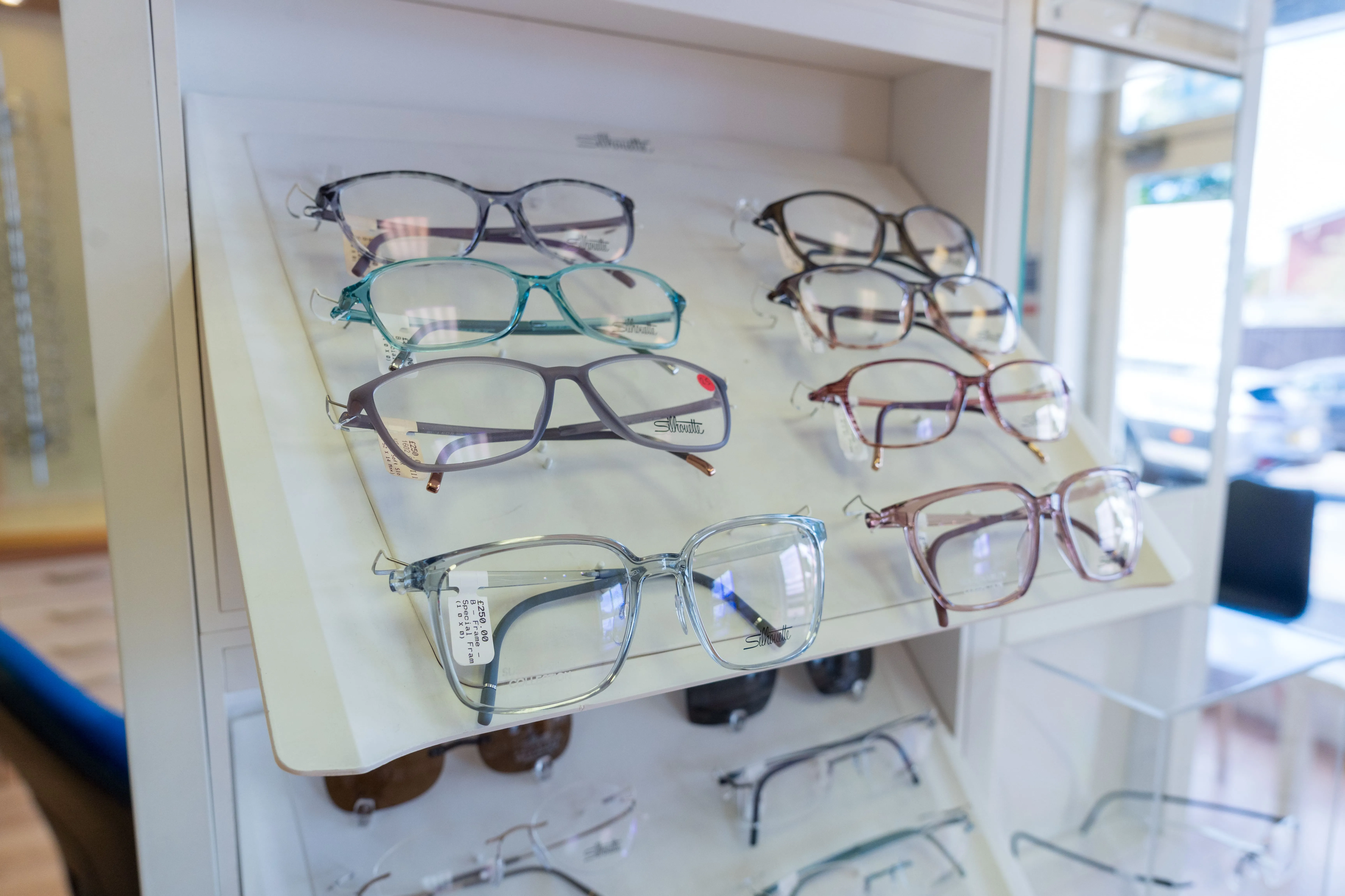 Display of various eyeglasses in different colors and styles on white shelves