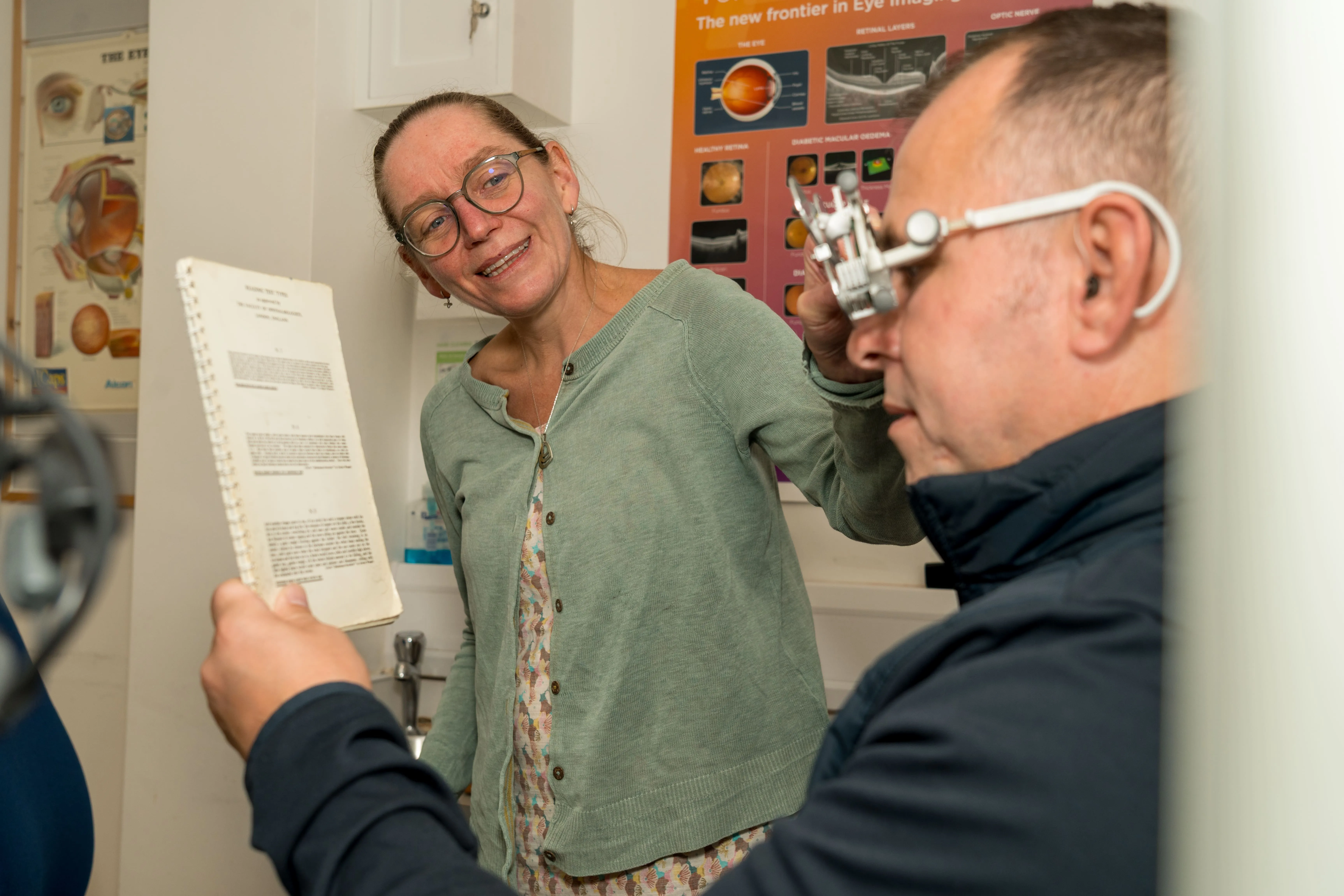 Optometrist examining patient with eye imaging poster in background