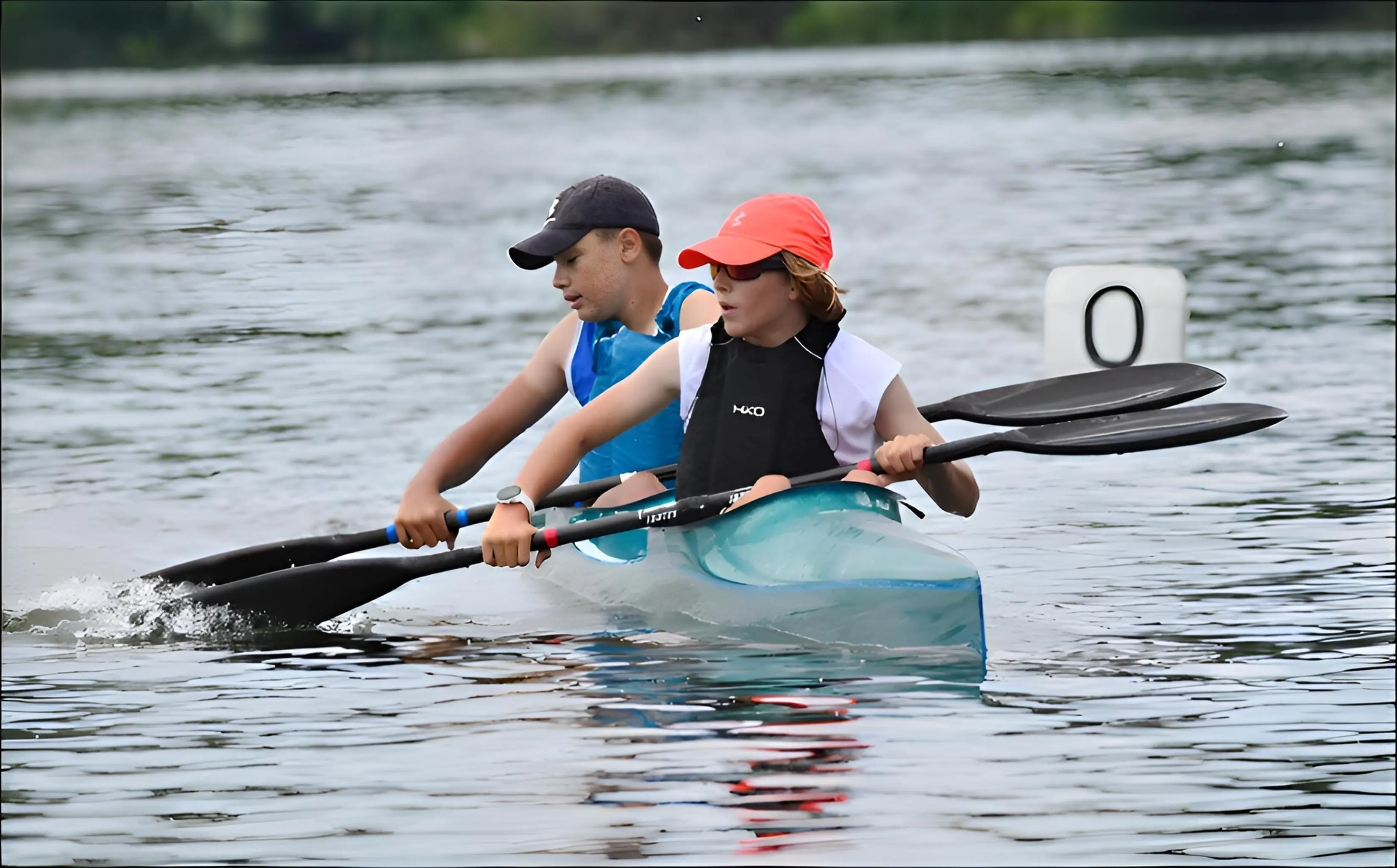 Two young kayakers paddling together in a tandem kayak on calm water near a buoy marked zero.