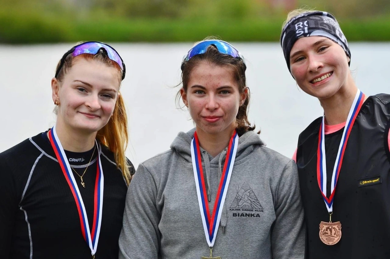 Three young female athletes wearing medals and sportswear, standing side by side and smiling.