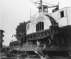Black and white photo of a large ship named Lipton docked at a pier with two people standing near the water.