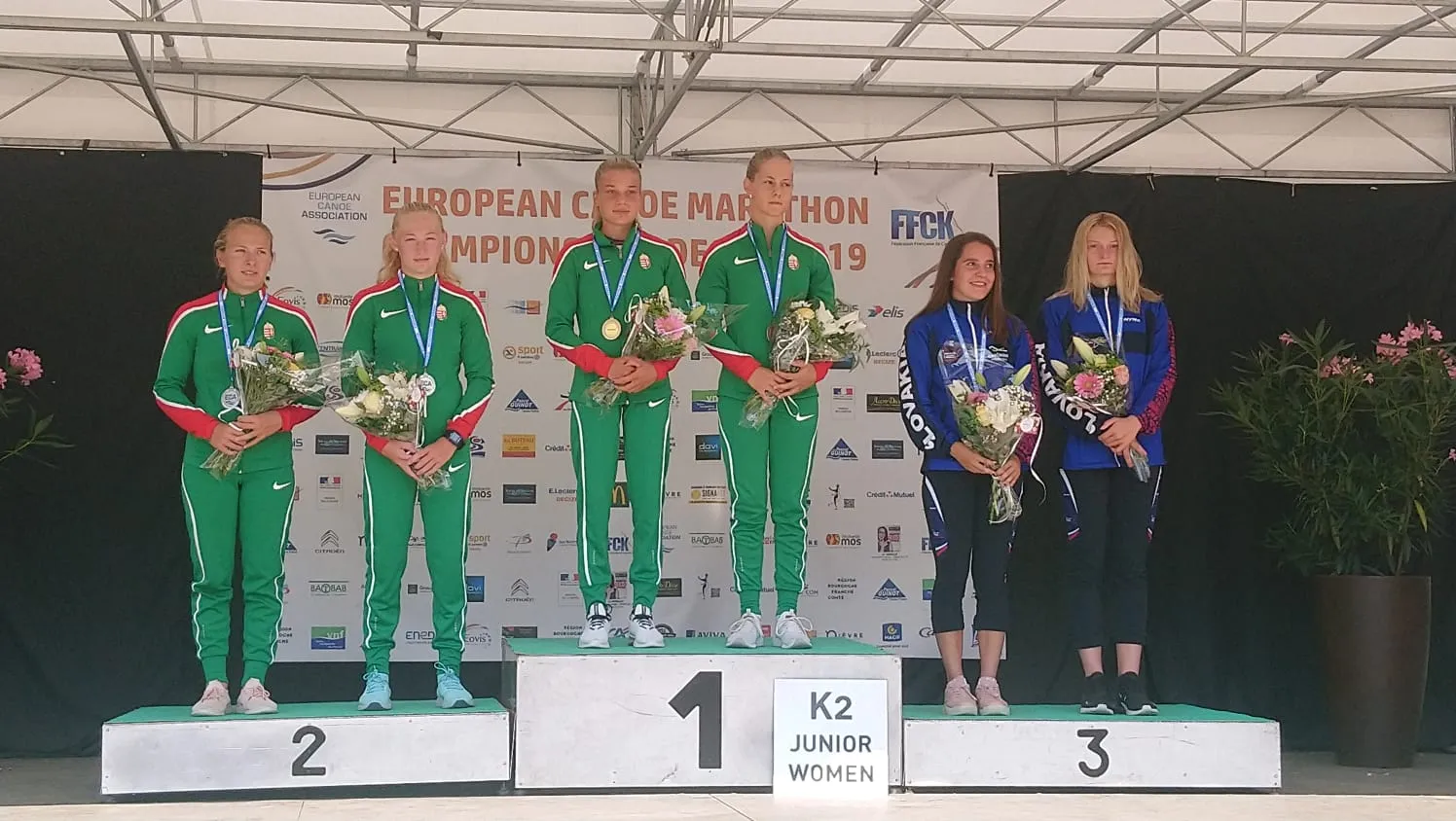 Six junior women athletes standing on a podium for K2 race winners at the European Canoe Marathon Championship 2019, holding flowers and medals.