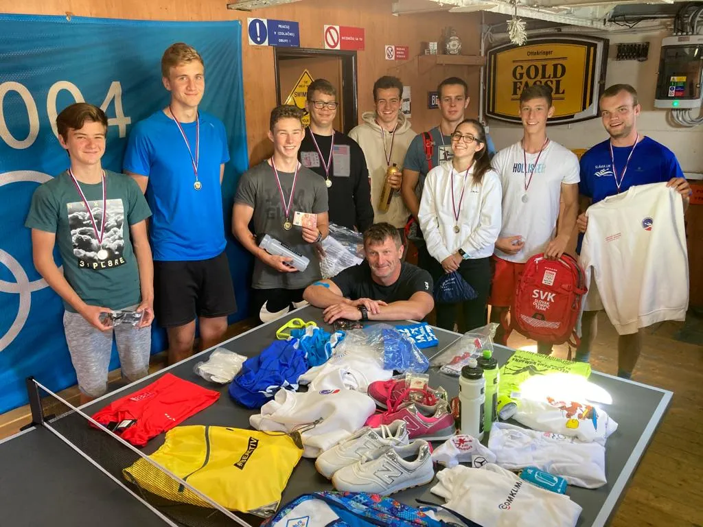 Group of young athletes wearing medals standing behind a table with sports gear and apparel, posing indoors.