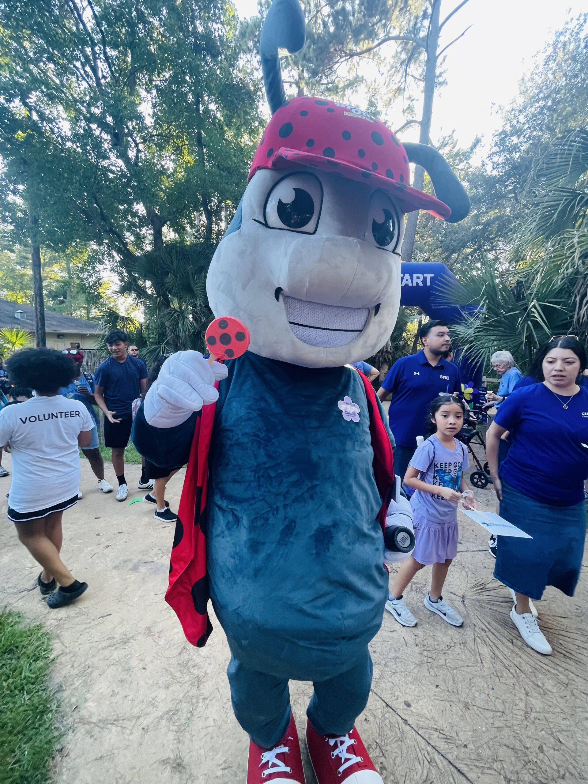 Ladybug mascot holding a lollipop outside.