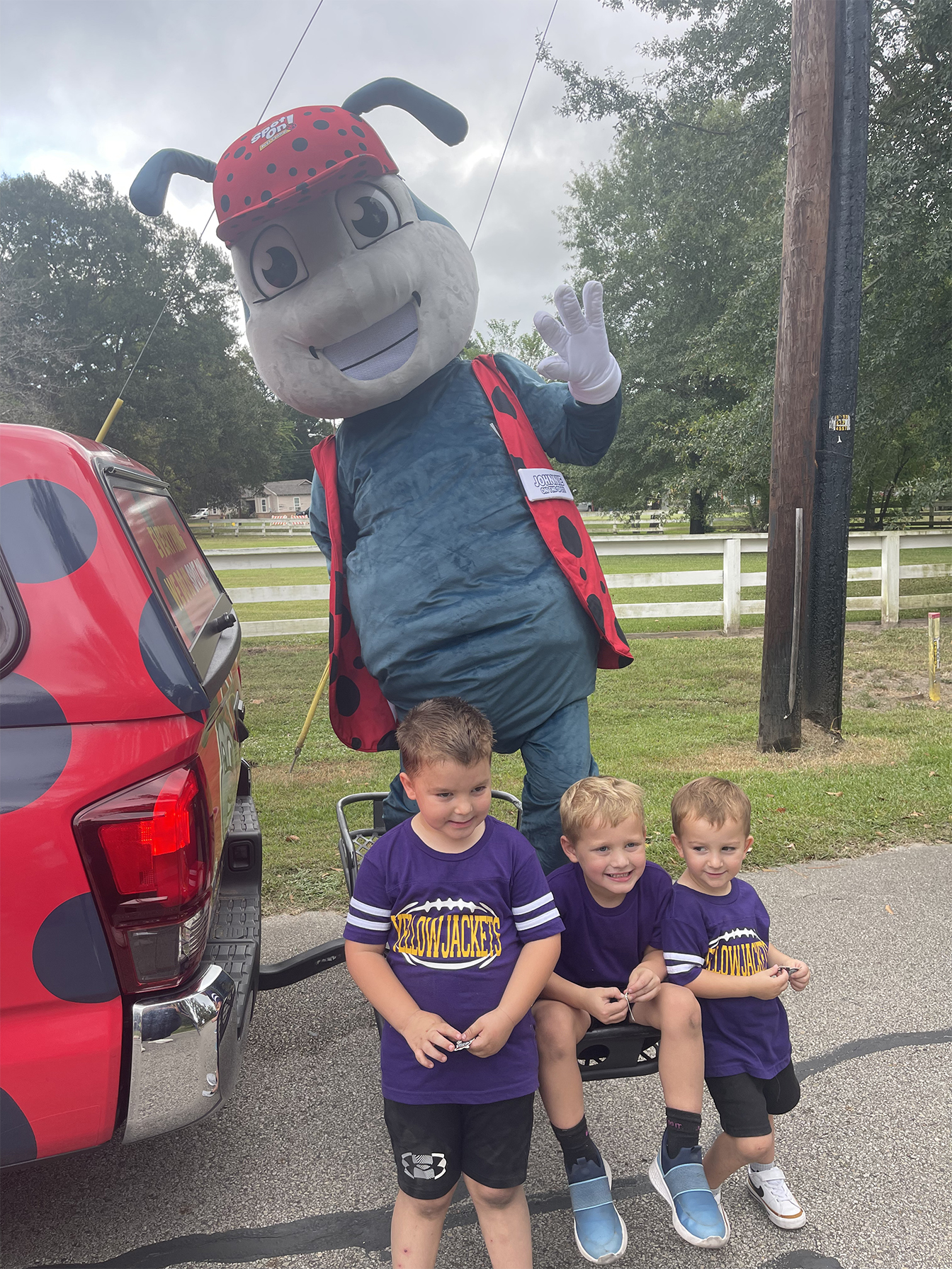 Mascot waves at three smiling boys.