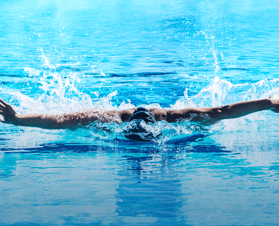Swimmer in a blue pool performing the butterfly stroke causing water to splash around.