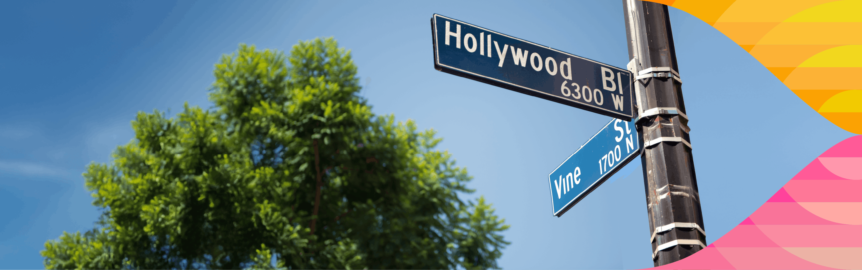 Intersection street signs of Hollywood Blvd and Vine St against a clear blue sky with green tree foliage nearby.