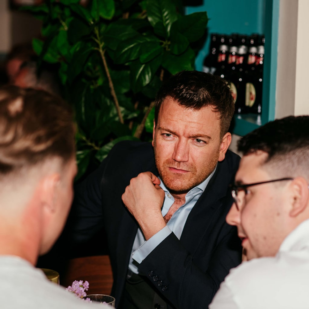 A man in a suit listening to conversation with two other men at a table