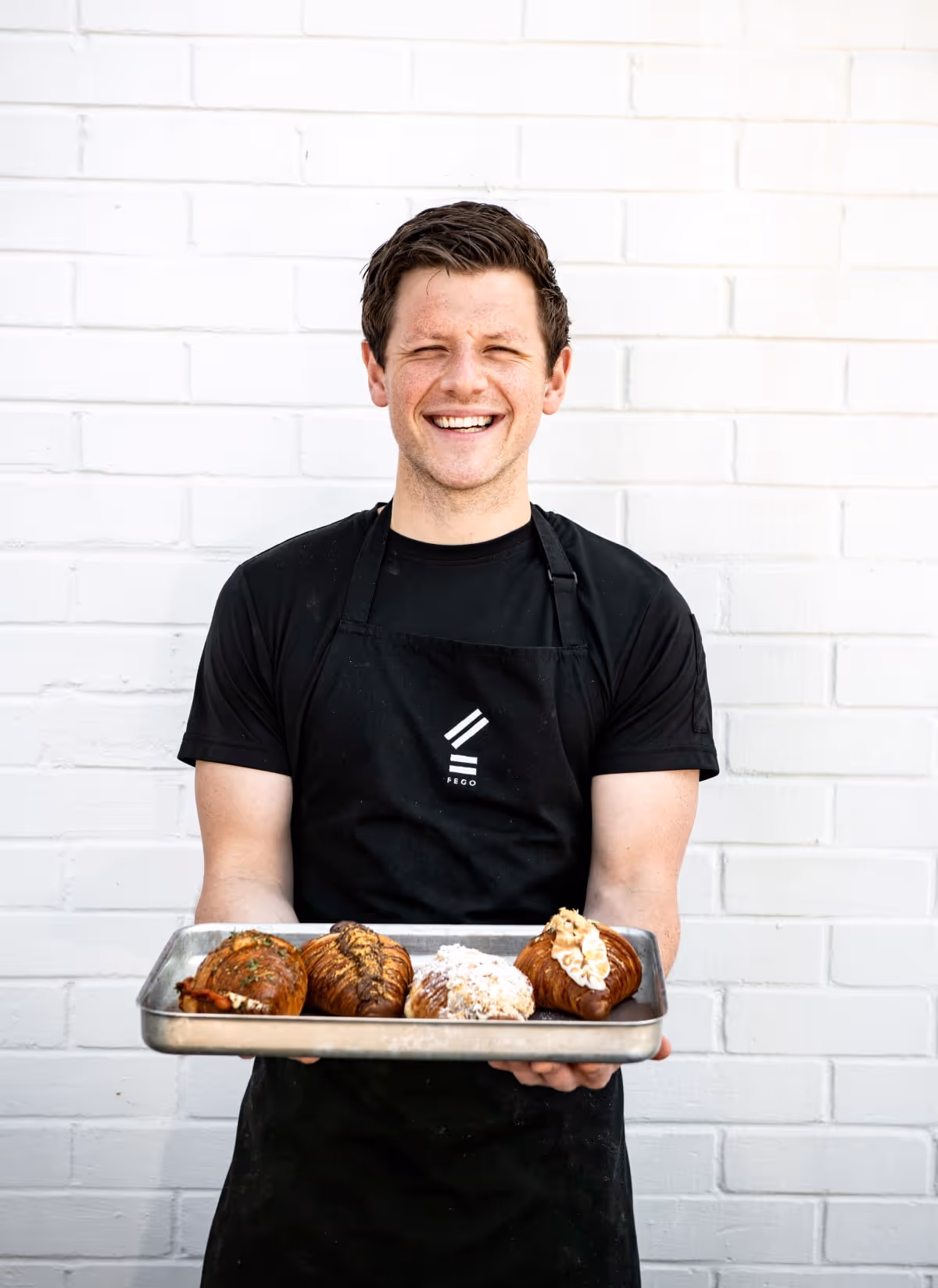 A Fego chef holding out a platter with pastries