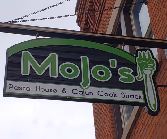 Outdoor hanging sign for Mojo's Pasta House & Cajun Cook Shack with a green fork graphic.