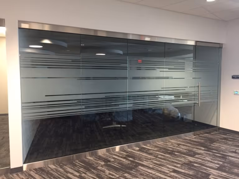 Office room with glass walls featuring horizontal frosted privacy stripes and a metal handle on the door.