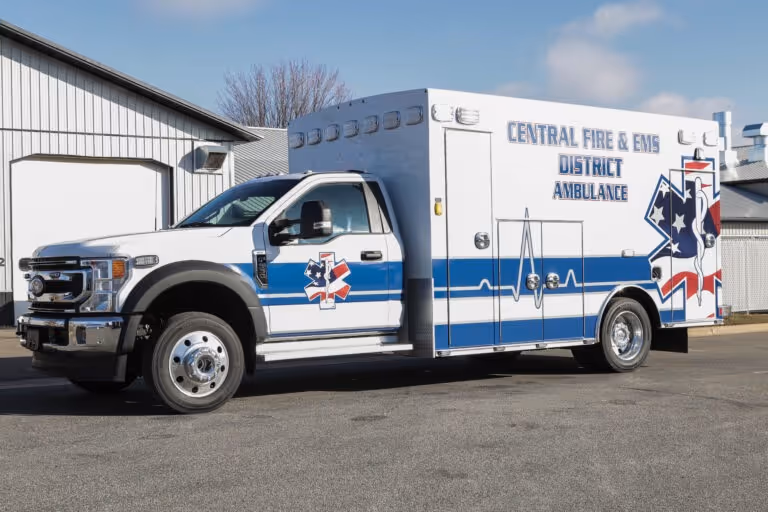 White and blue ambulance with Central Fire & EMS District Ambulance text parked outside a building.