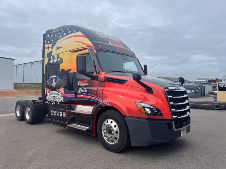 Red and black semi-truck with a patriotic military-themed mural showing an American flag, soldiers, and aircraft on the side.