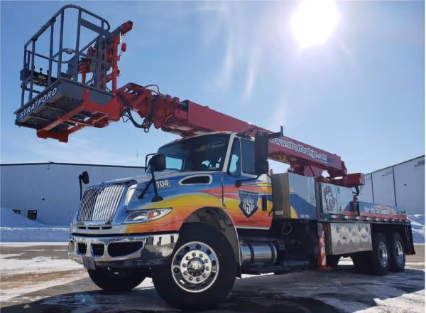 Large utility truck with an extended red hydraulic lift platform under a clear blue sky.