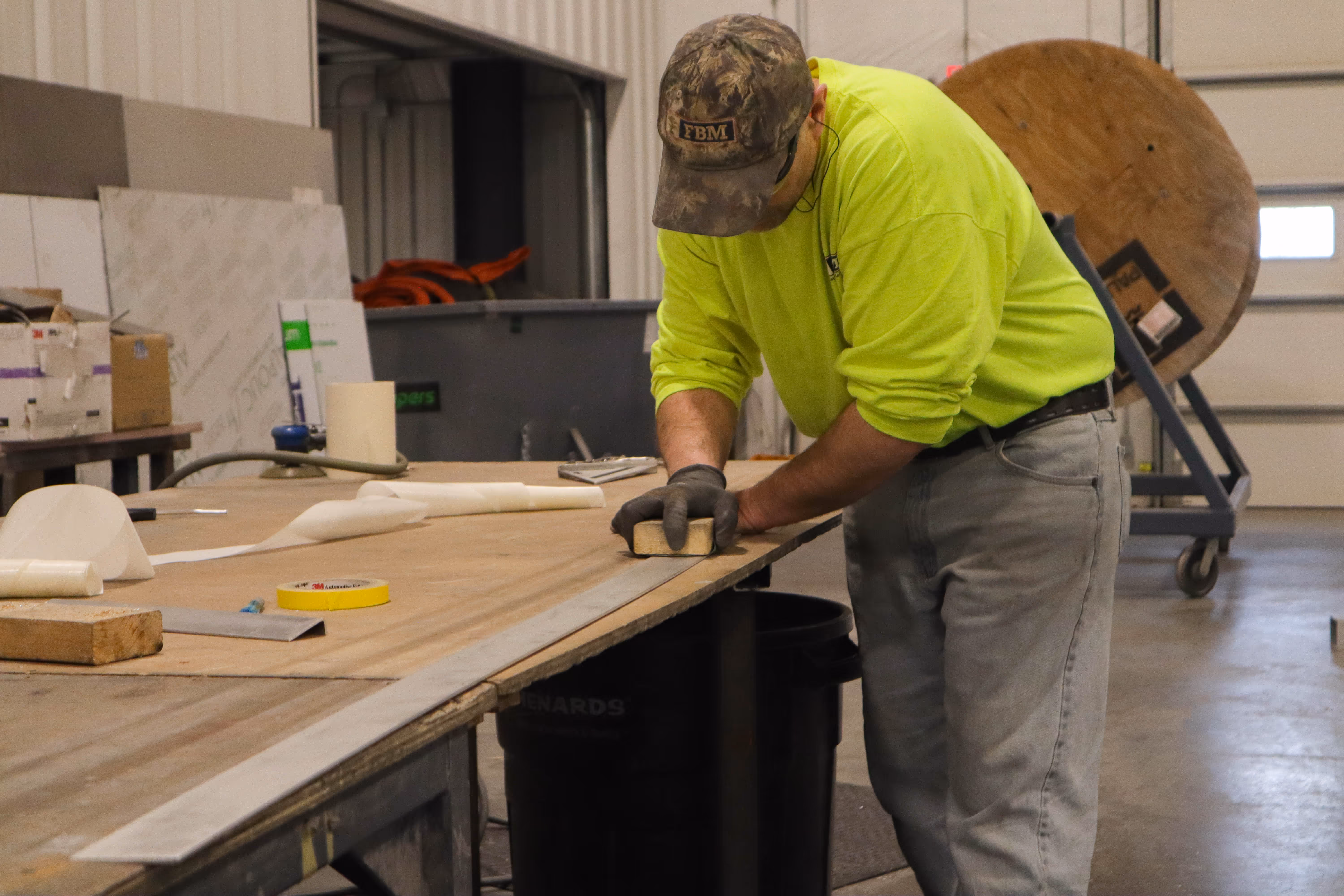 A man wearing a yellow shirt is working on a wooden table.