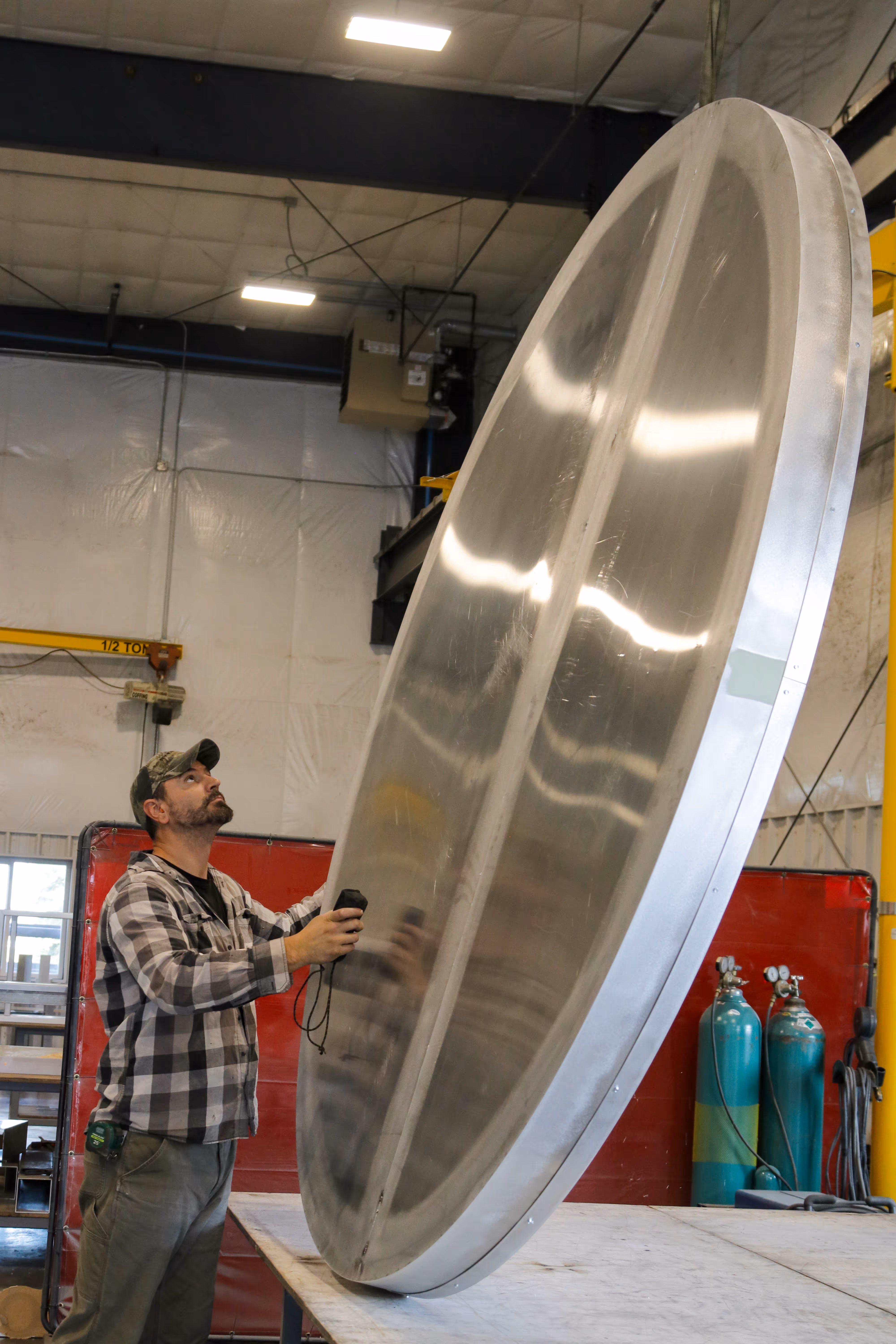 A man is holding a large metal disk in a factory.