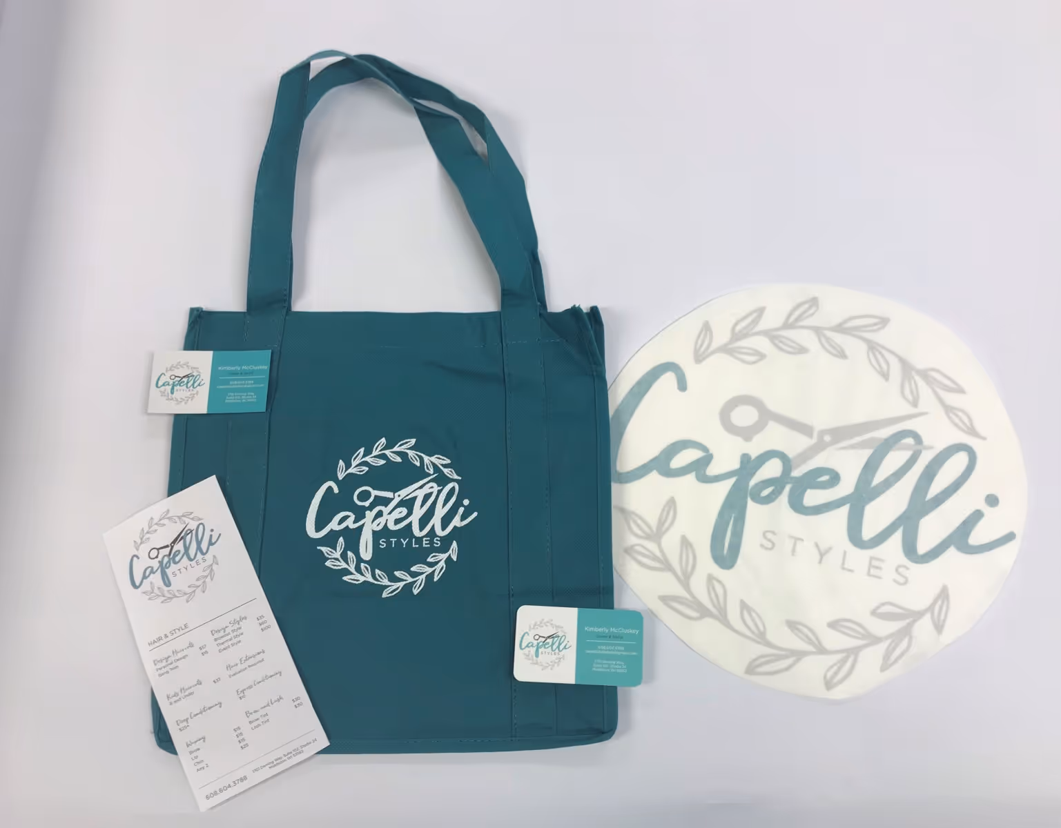 Teal tote bag with a white 'Capelli Styles' logo, accompanied by matching business cards and a price list.