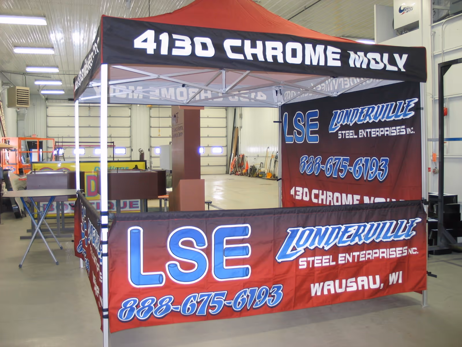 Red and black promotional tent for Londerville Steel Enterprises with phone number and address inside a warehouse.