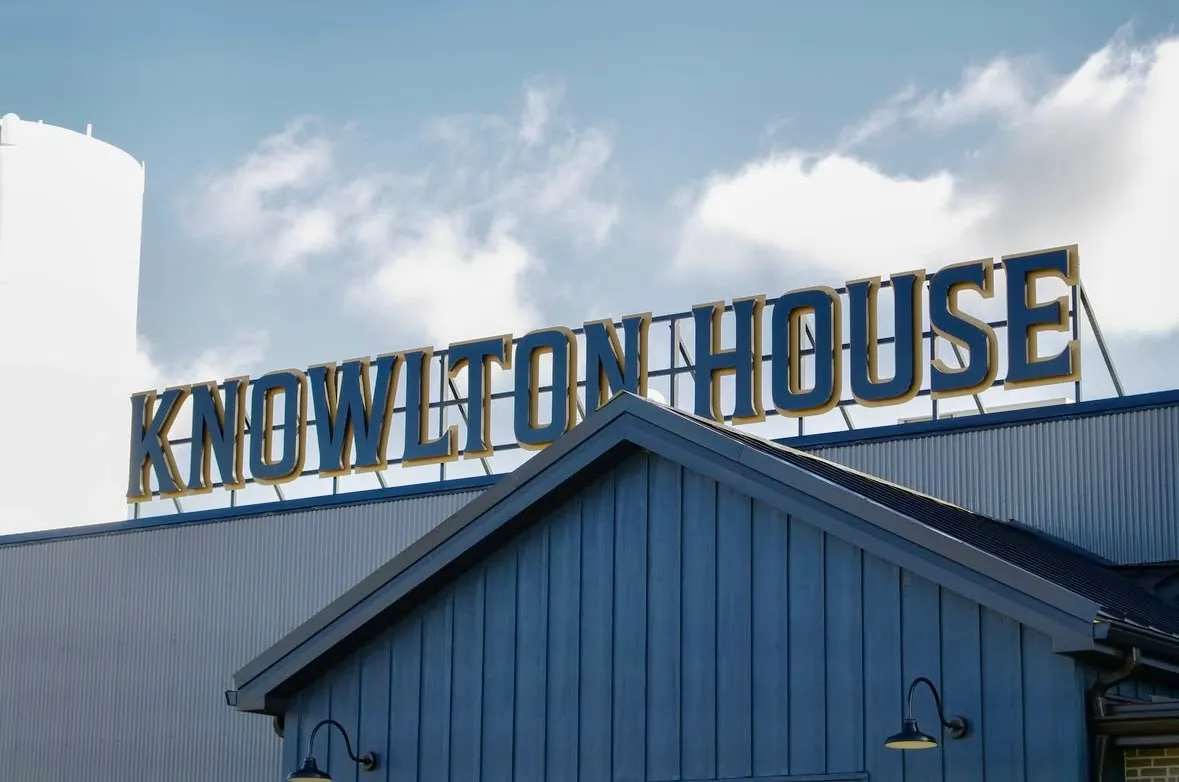 Large sign reading 'KNOWLTON HOUSE' mounted on top of a blue-gray building under a partly cloudy sky.