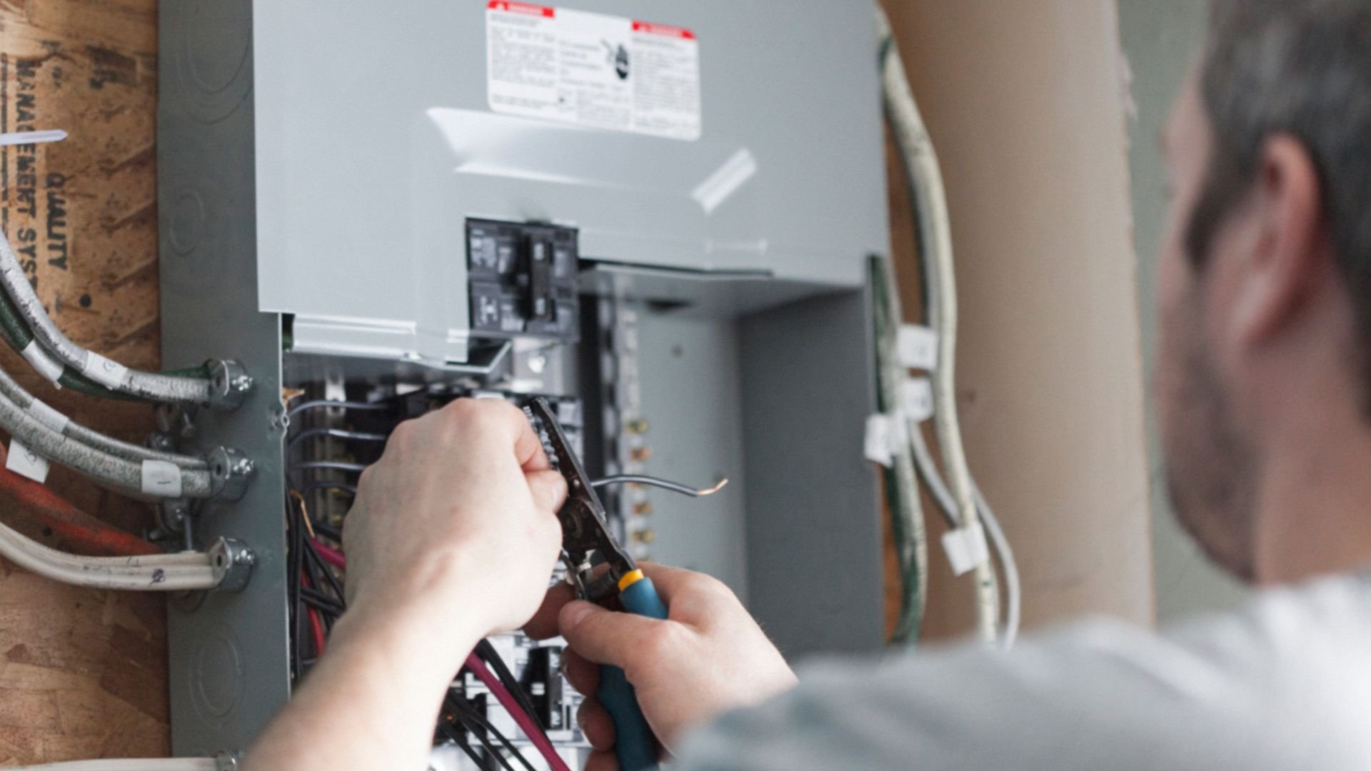 Electrician working on electrical panel with screwdriver and exposed wires