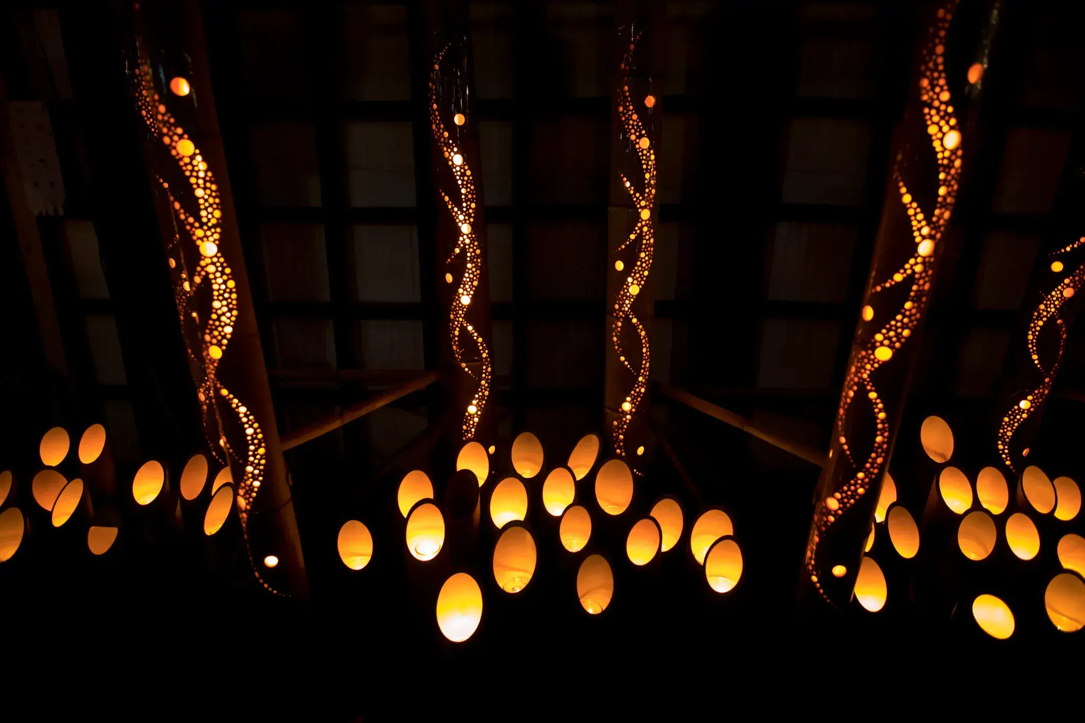 An array of decorative pendant lights with perforated, organic shapes hang from a ceiling, casting a warm orange glow.