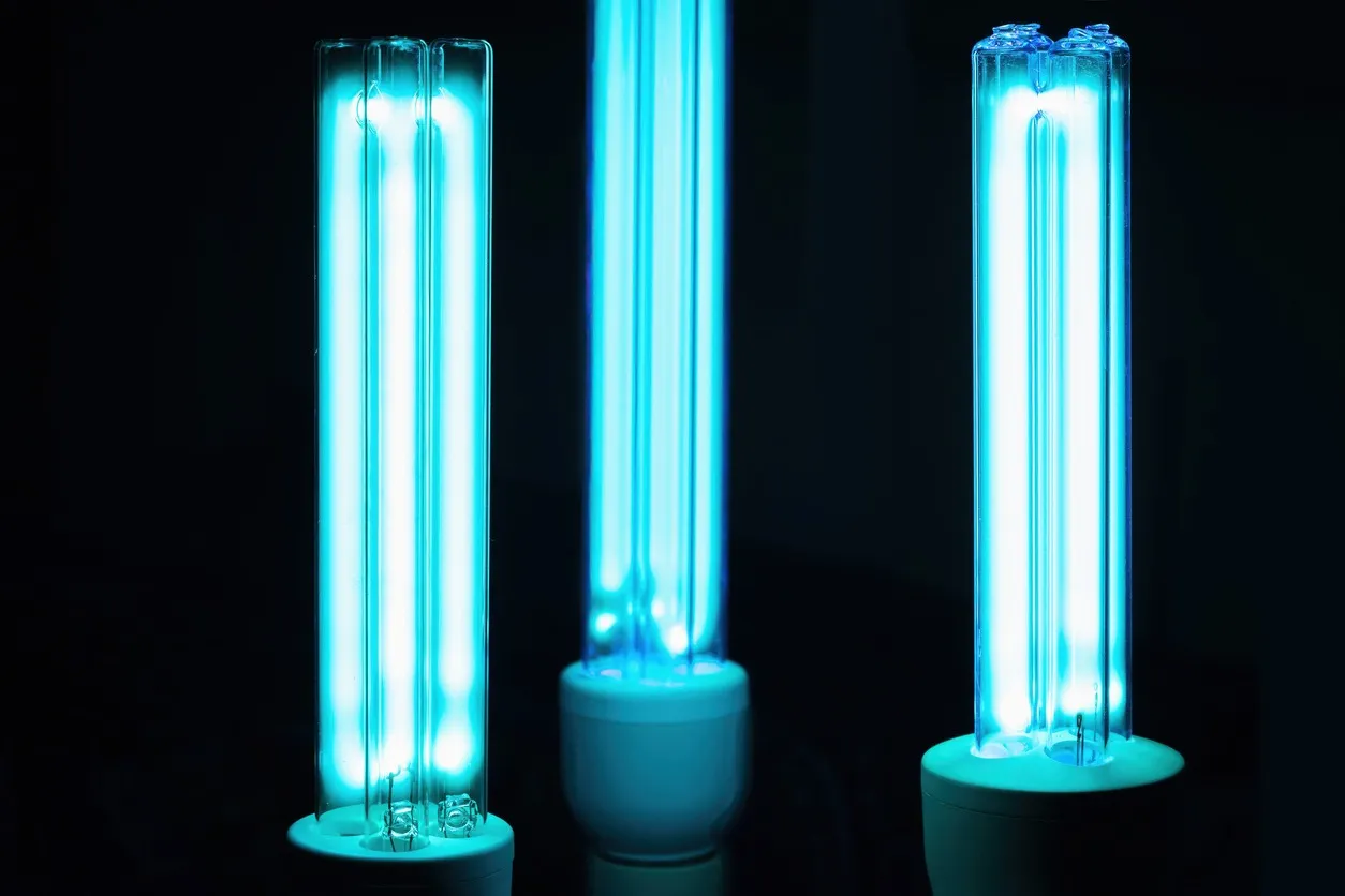 Three glowing ultraviolet light bulbs, also called germicidal lamps, stand vertically against a black background