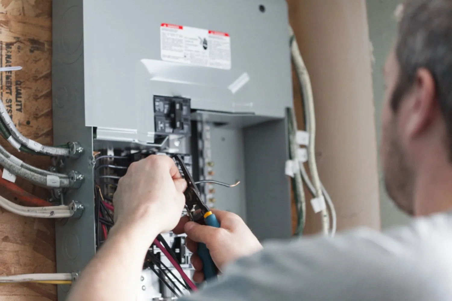 A close-up shot of a man wearing a gray shirt, carefully working on an electrical panel.