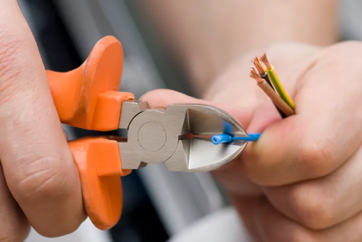A close-up shot of a person's hands using wire strippers to cut and strip the insulation from a group of electrical wires.