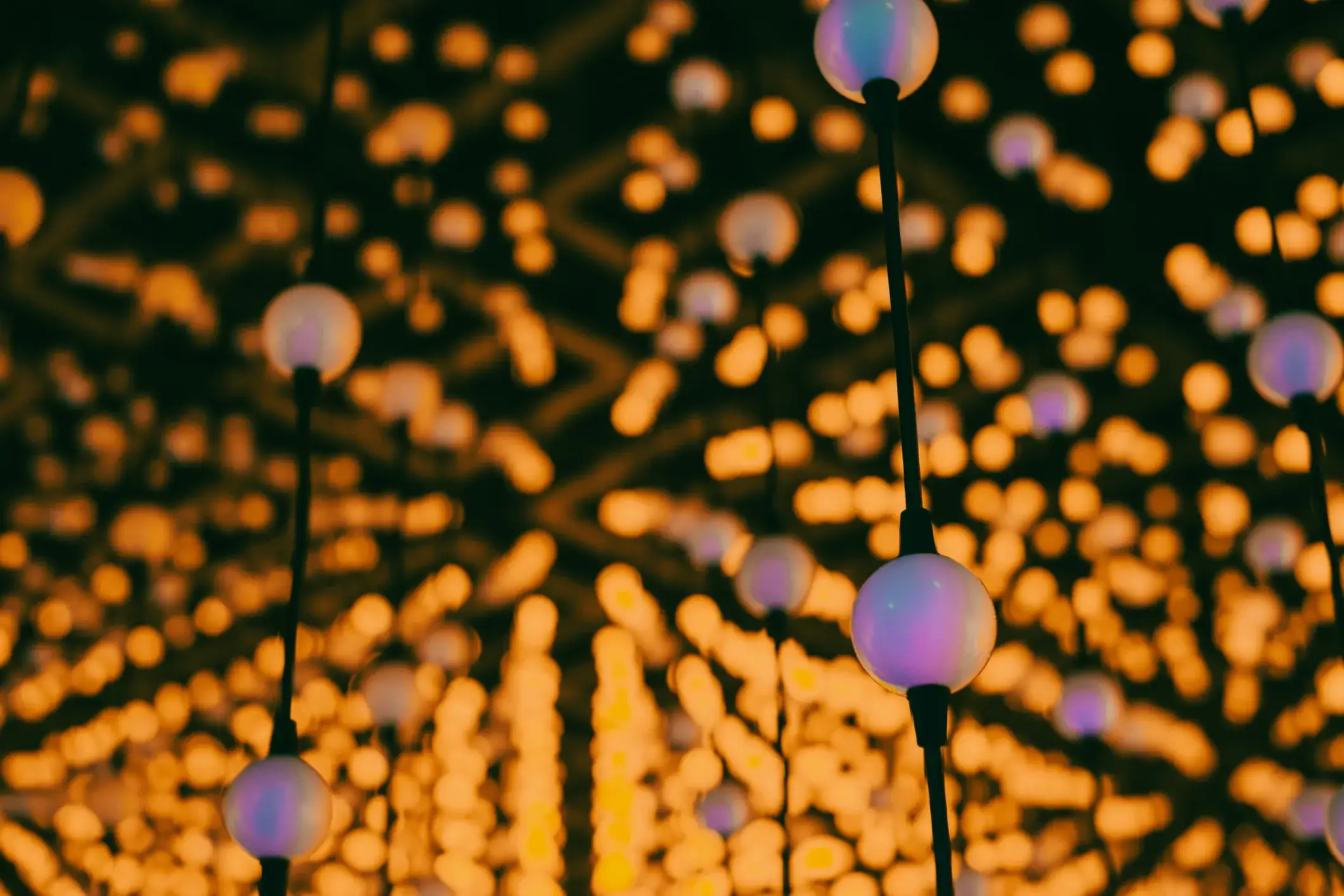 A close-up, abstract image of glowing spherical lights hanging from black cords against a background of blurred, orange bokeh.
