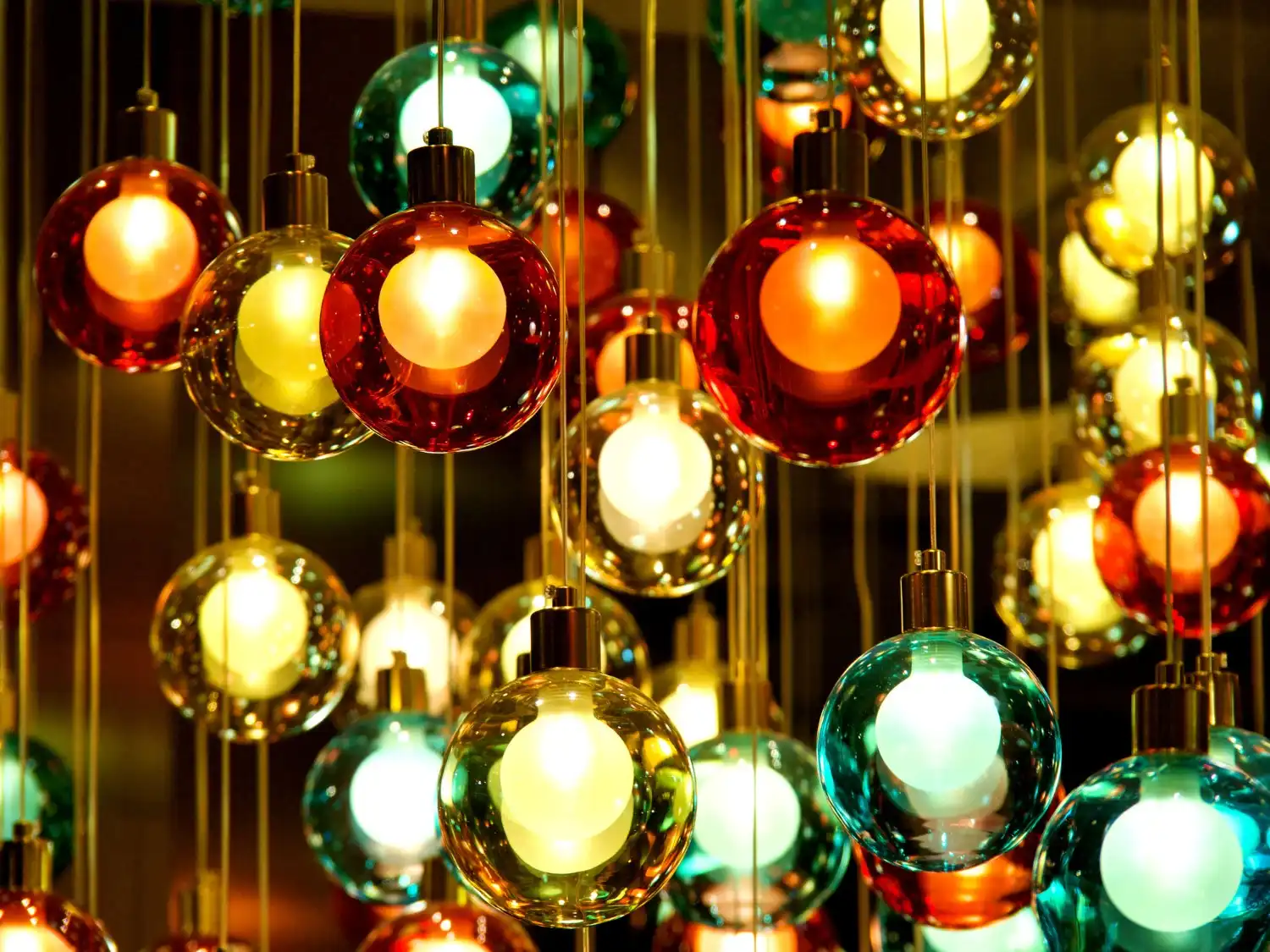 A large, modern chandelier composed of a cascading cluster of clear and colored glass globes with internal lights, creating a warm, vibrant glow.