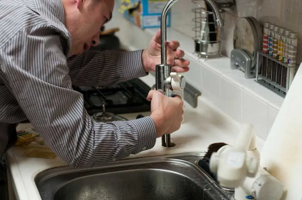 A person installs a kitchen faucet.