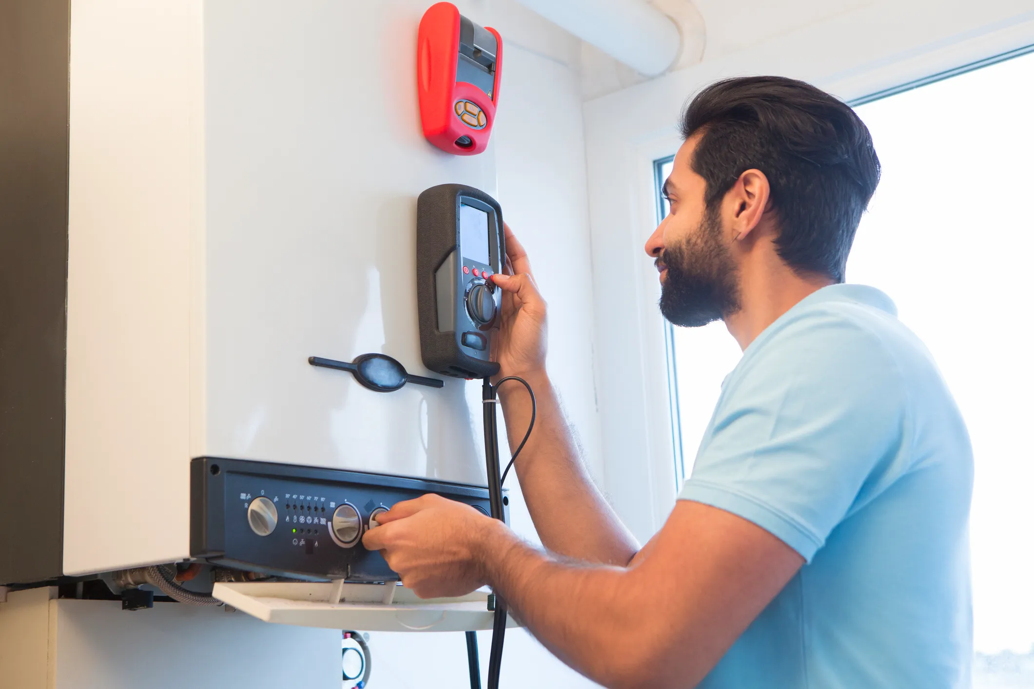 Plumber using a multimeter to test a boiler's electrical components.