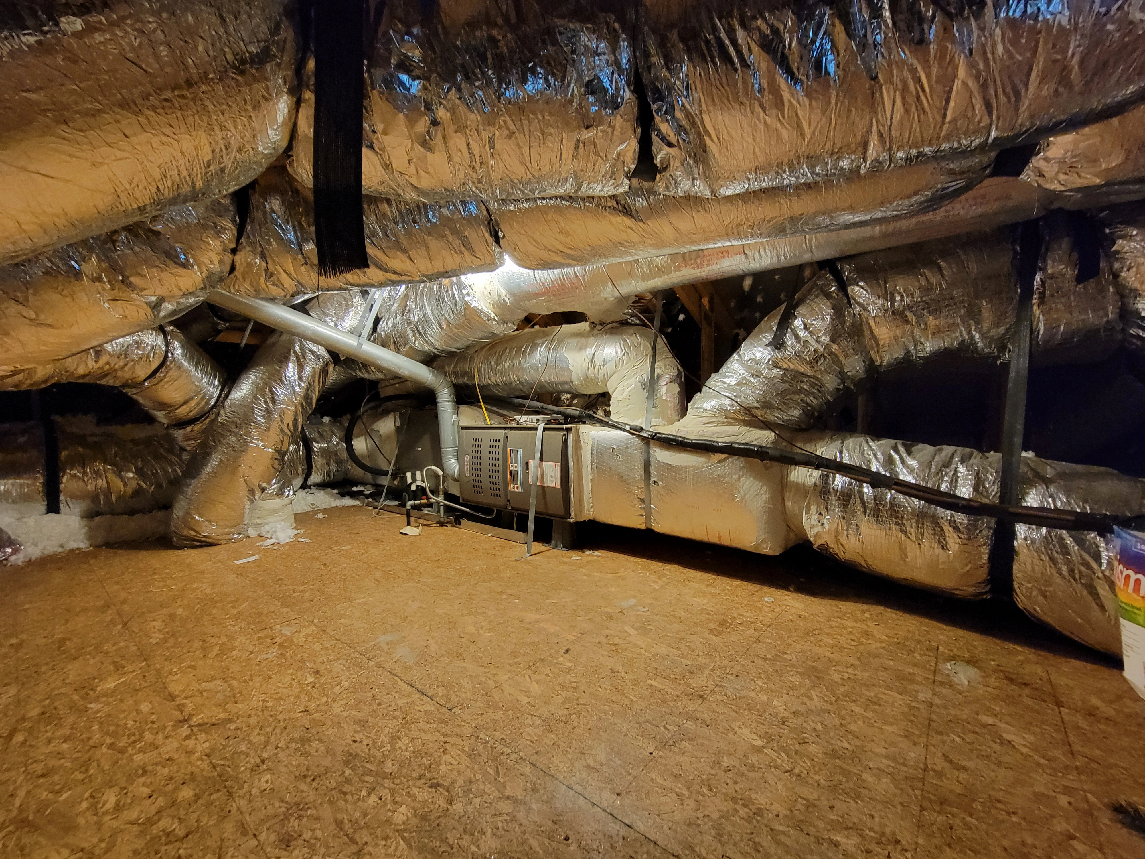 Attic with exposed HVAC system, featuring large silver insulated ducts and a central unit.