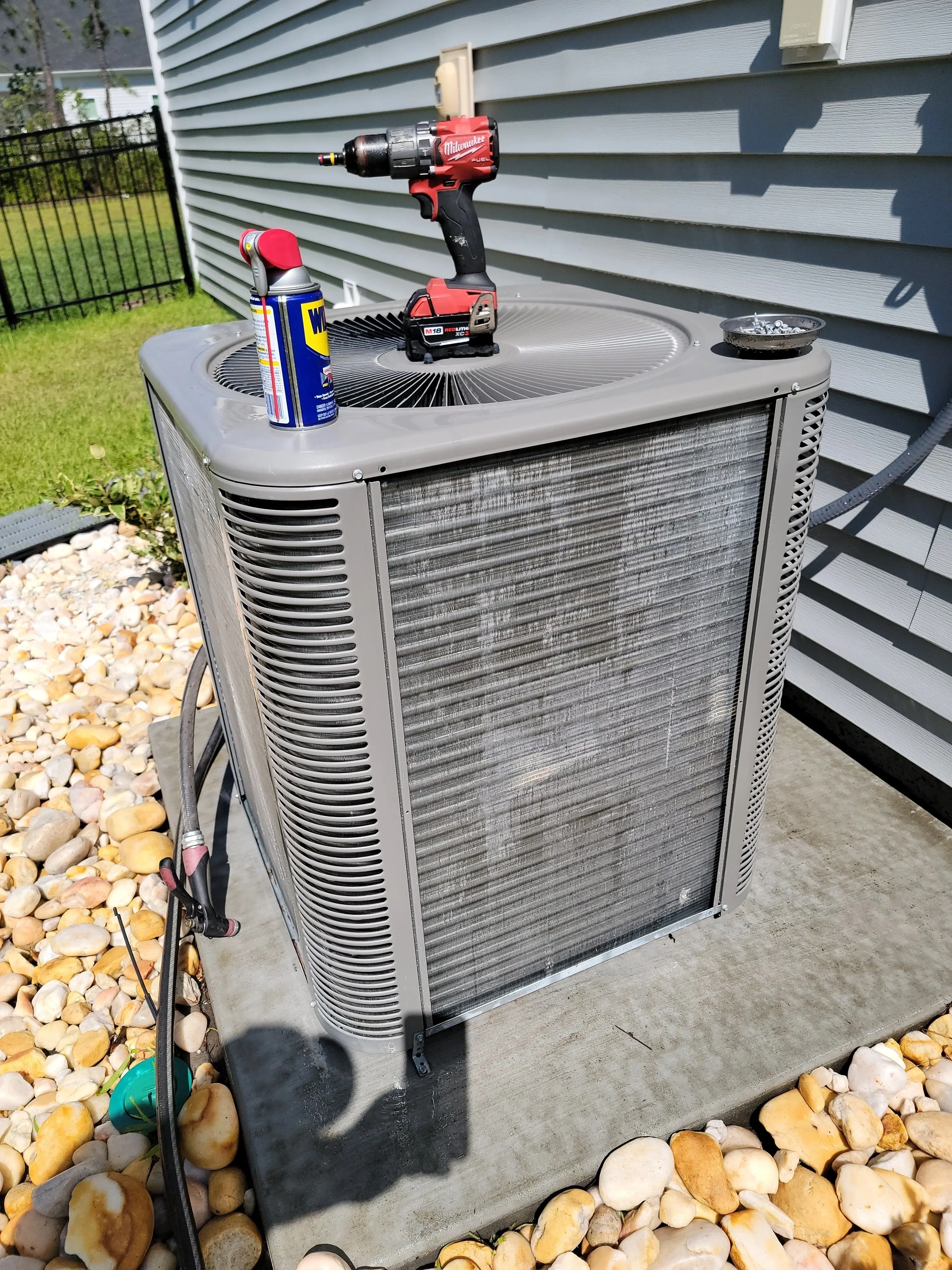 Outdoor air conditioning unit on a concrete slab, with a drill and a can of lubricant on top.