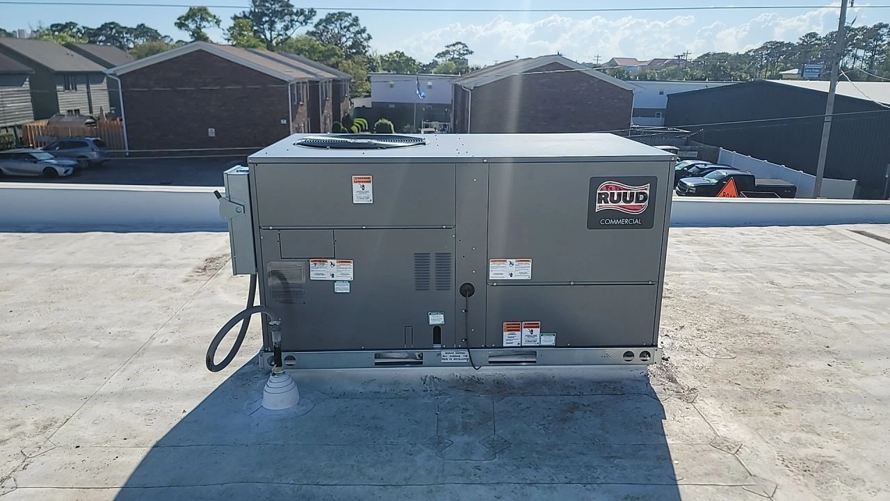 Rooftop HVAC unit under clear sky on a flat white roof. Background shows residential and commercial buildings