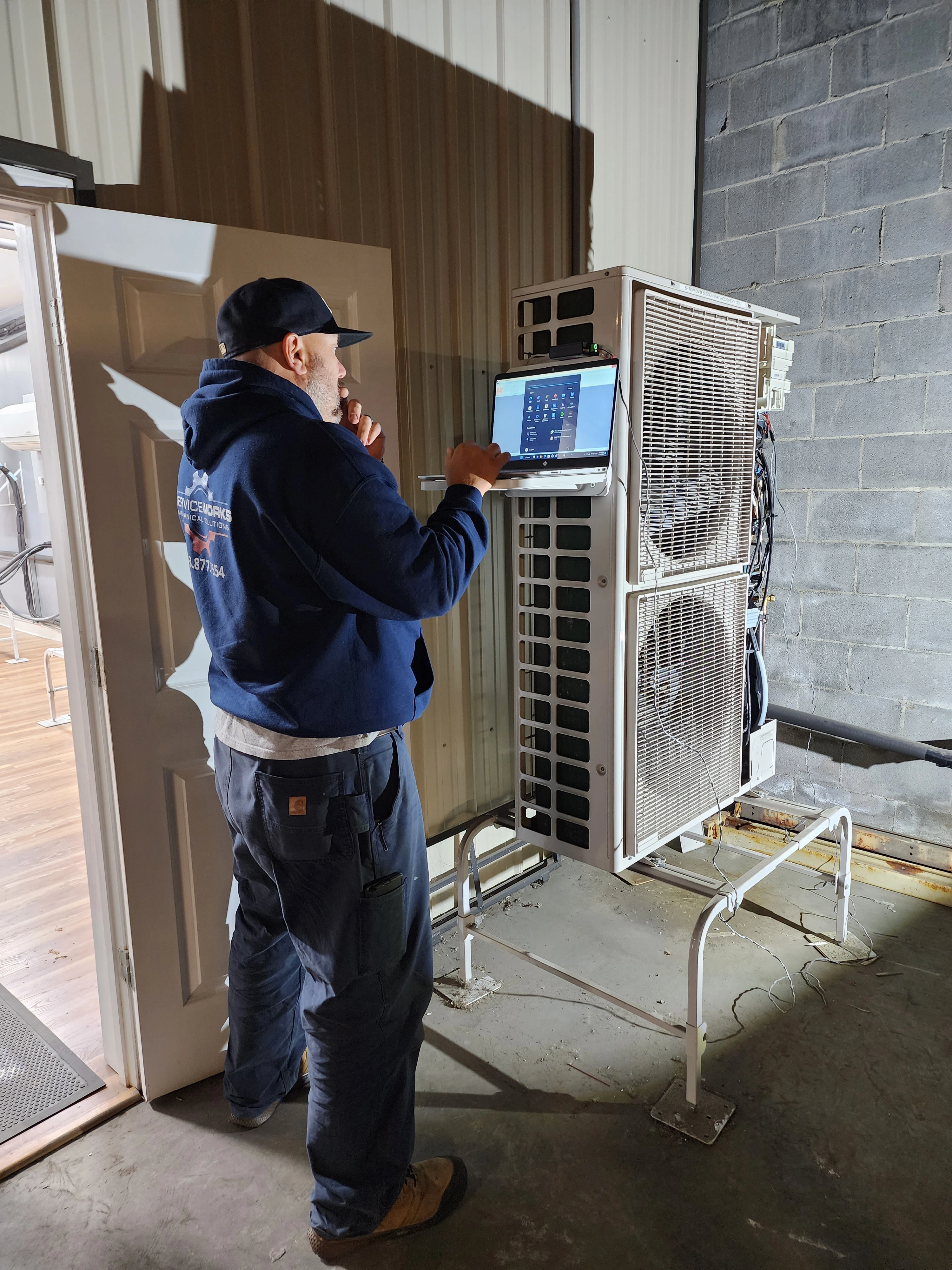 A man stands beside a large mini-split air conditioner, showcasing its size and design in a well-lit environment.