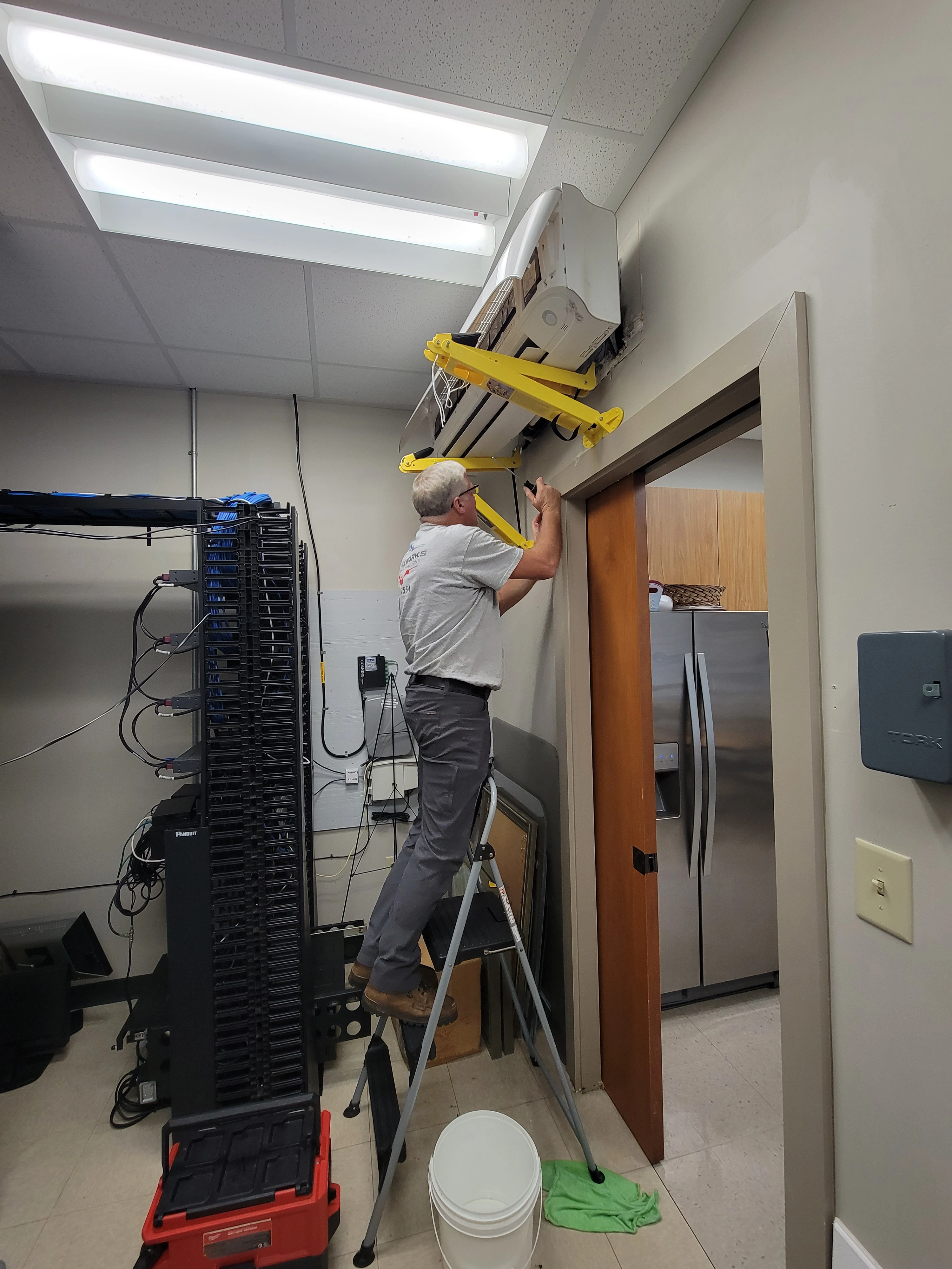 A man installs a mini split unit by hanging it from the ceiling during a replacement process.