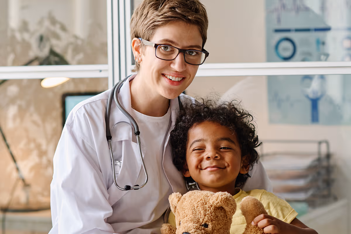 Pediatric doctor with stethoscope smiling with happy child holding teddy bear at a healthcare clinic