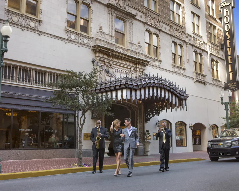Beautiful couple walking with jazz musicians in front of the Roosevelt Hotel in New Orleans, LA