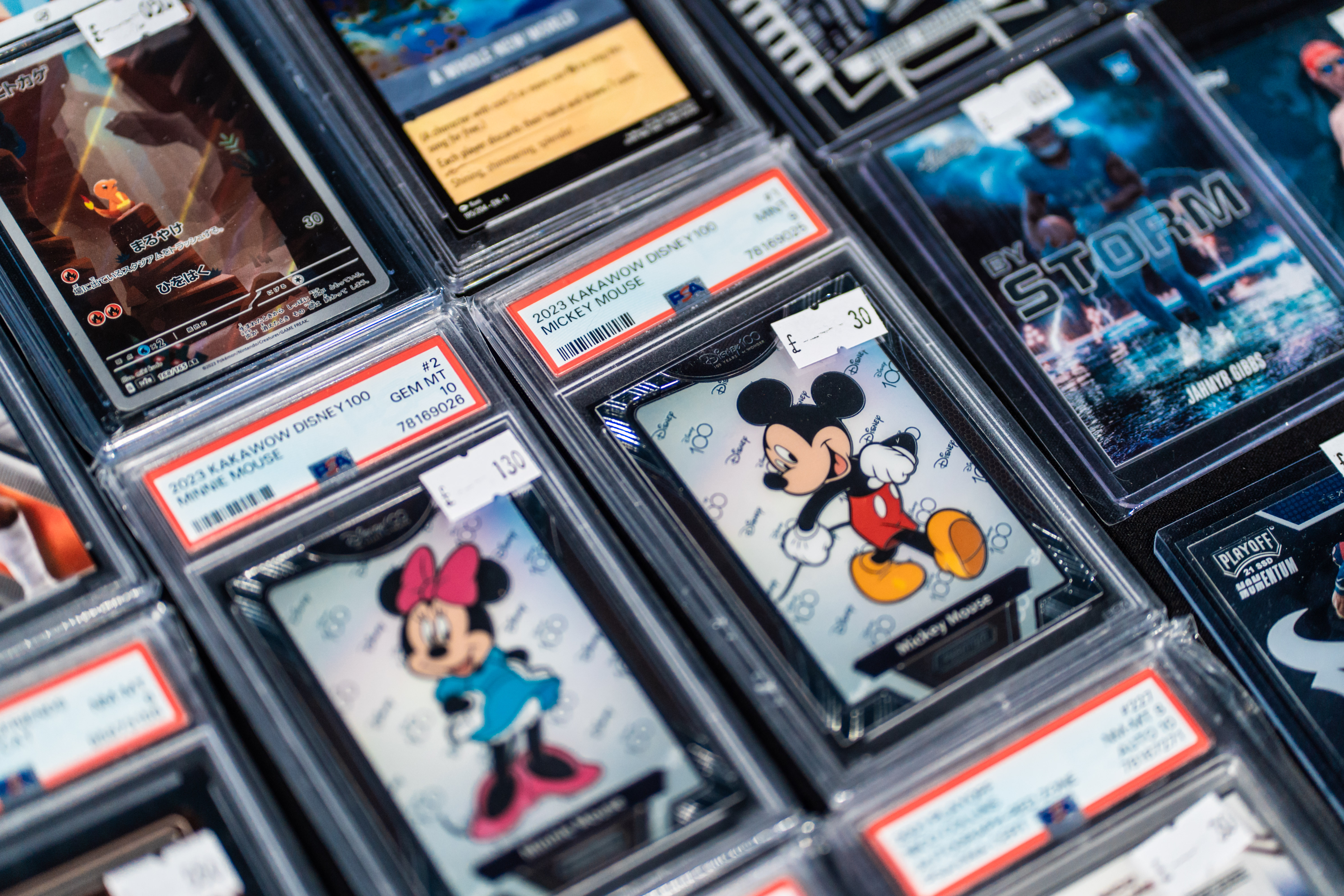 A man helps a young boy browse trading cards at a convention, looking through binders displayed on a table.