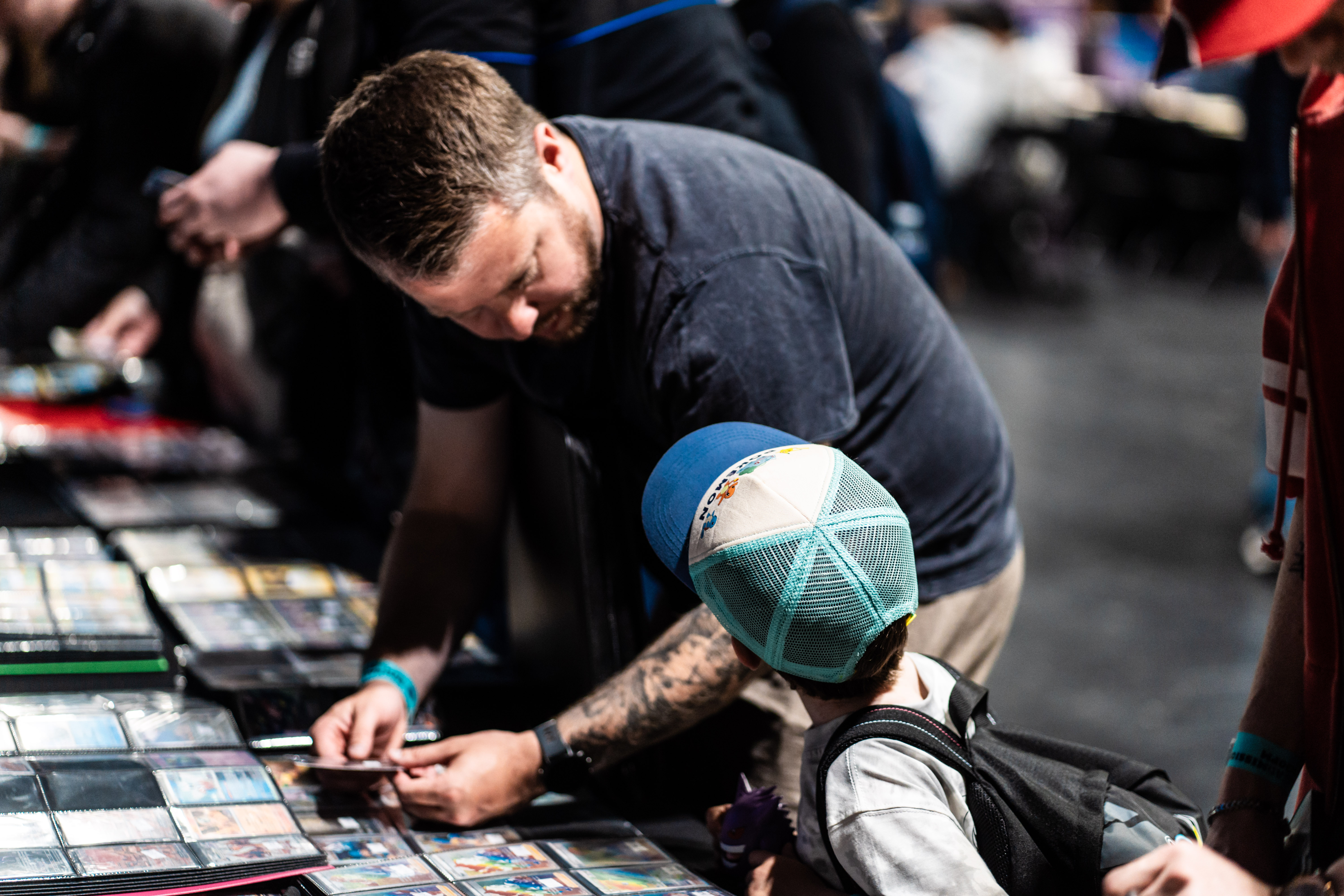 A man in a blue tracksuit browses rows of trading cards at a vendor stand during the convention.
