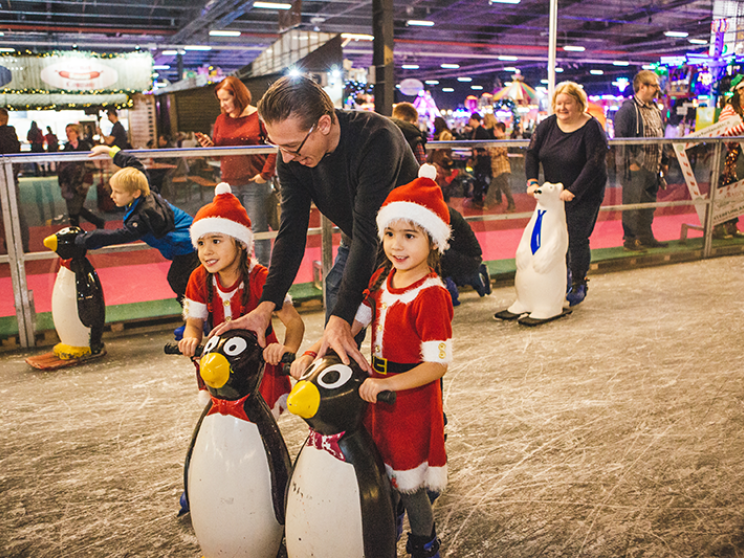 Two little girls on an ice rink skating with a penguin