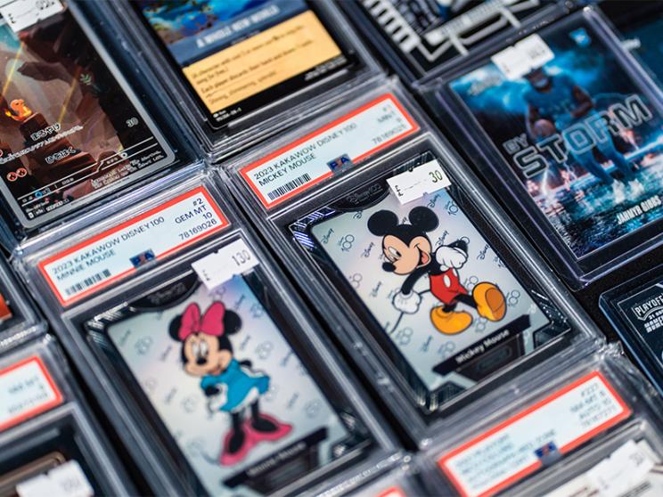 Close-up of various collectible trading cards in protective plastic cases, displayed on a table at a convention or marketplace.