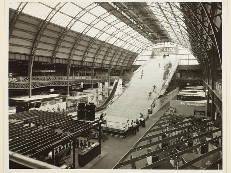 Black and white photo of Olympia London in 1976, showing a large indoor artificial ski slope for the International Ski Show.