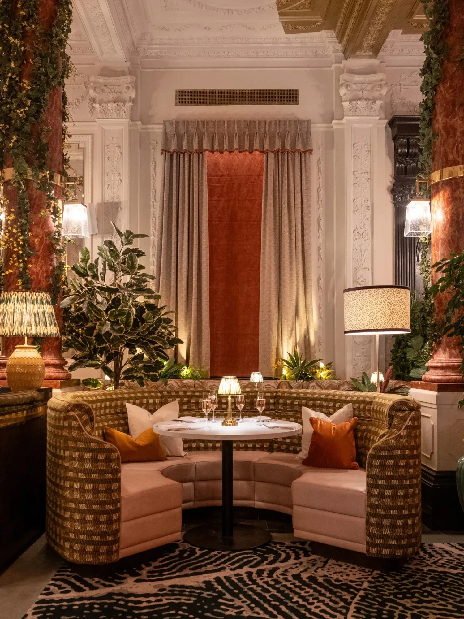 Interior of Idalia, a restaurant in Pillar Hall, Olymia - rounded chair with table in the centre. with Pillar Hall's iconic columns either side and greenery.