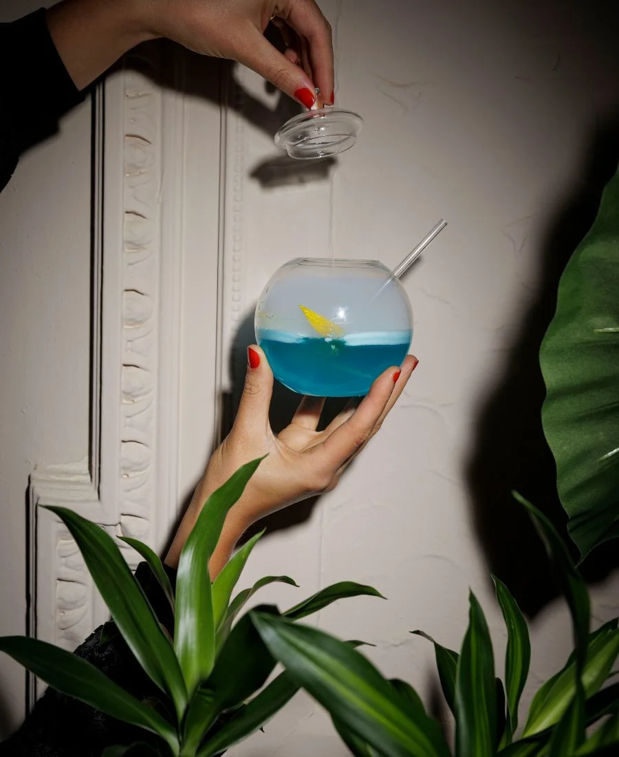 Blue cocktail at Idalia in round glass with lid being held.