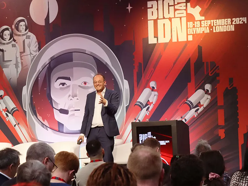 Man in a dark suit and white shirt speaking on stage in front of an audience at BIG DATA LDN 2024.